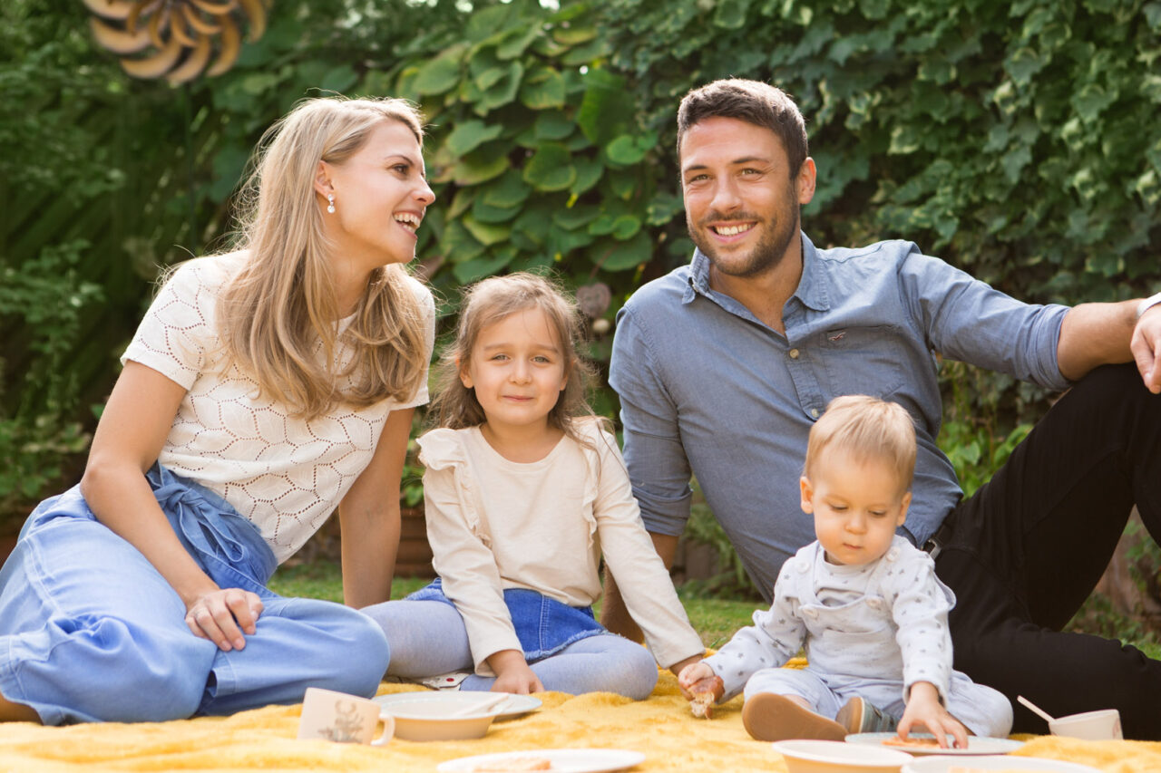Photovoltaik Familie sitzt gemeinsam im Garten auf einer gelben Decke - Klarsolar